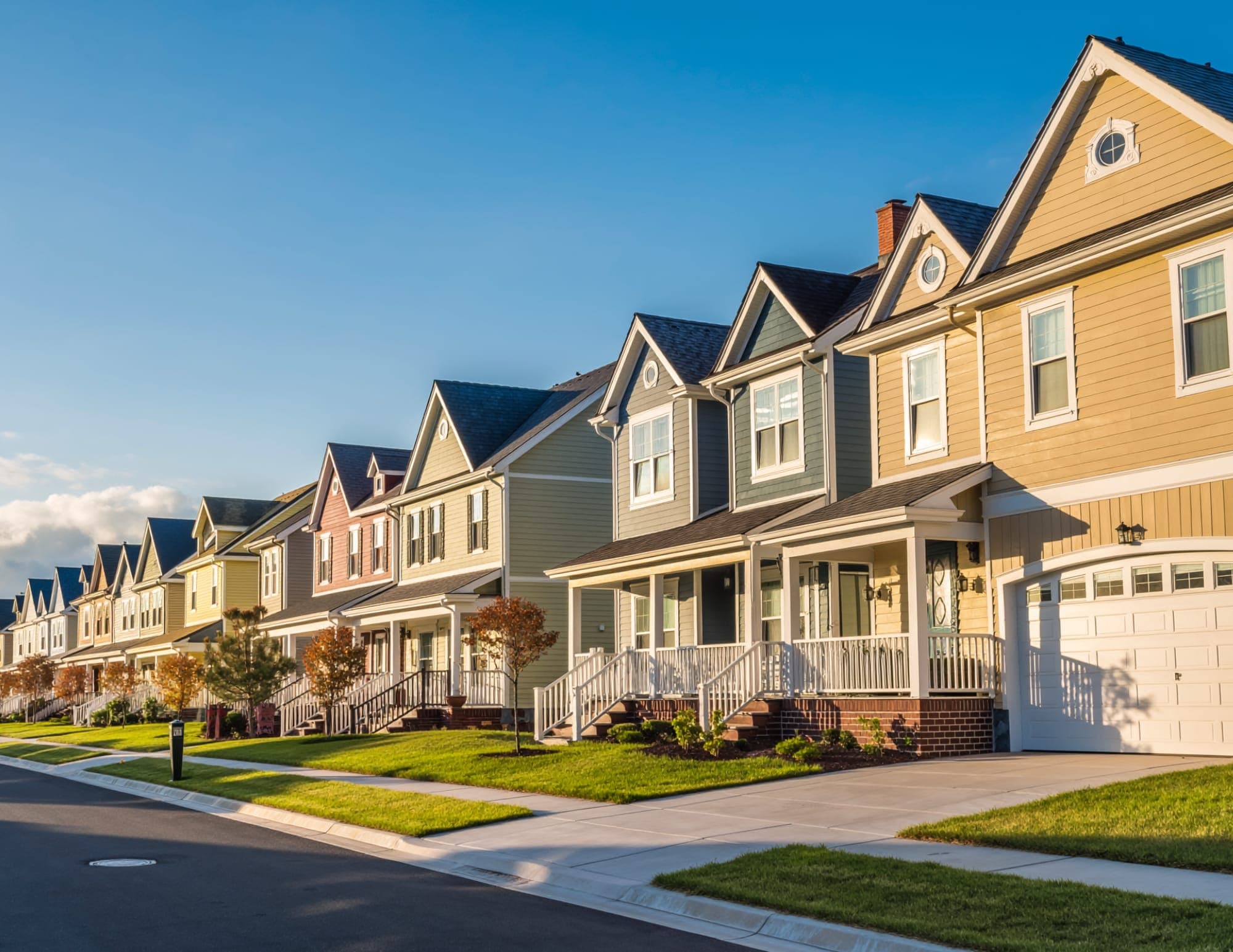 Row of colorful two-story suburban homes with covered front porches along a tree-lined street at golden hour