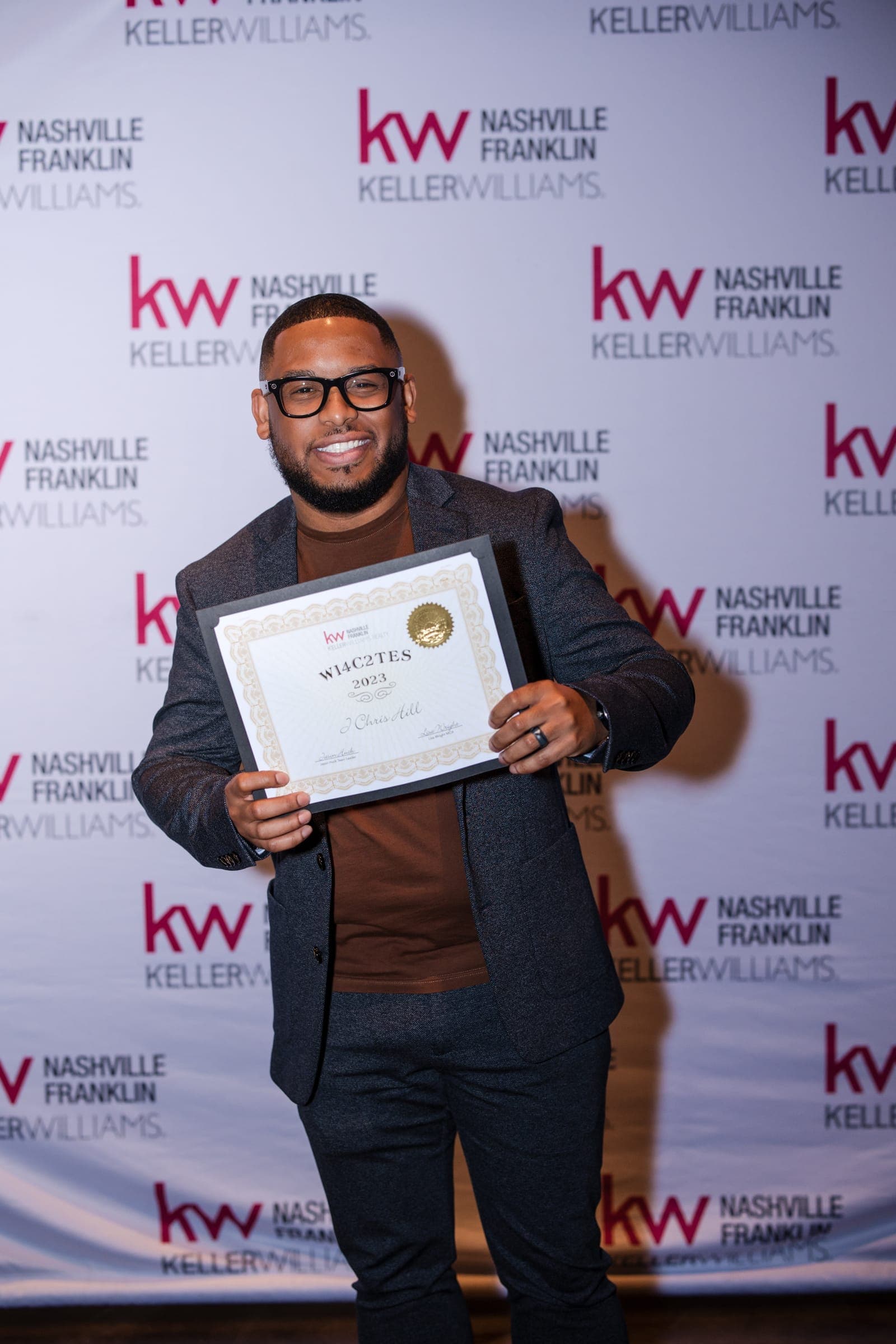 An agent beaming with a framed achievement certificate at the Franklin awards night step-and-repeat