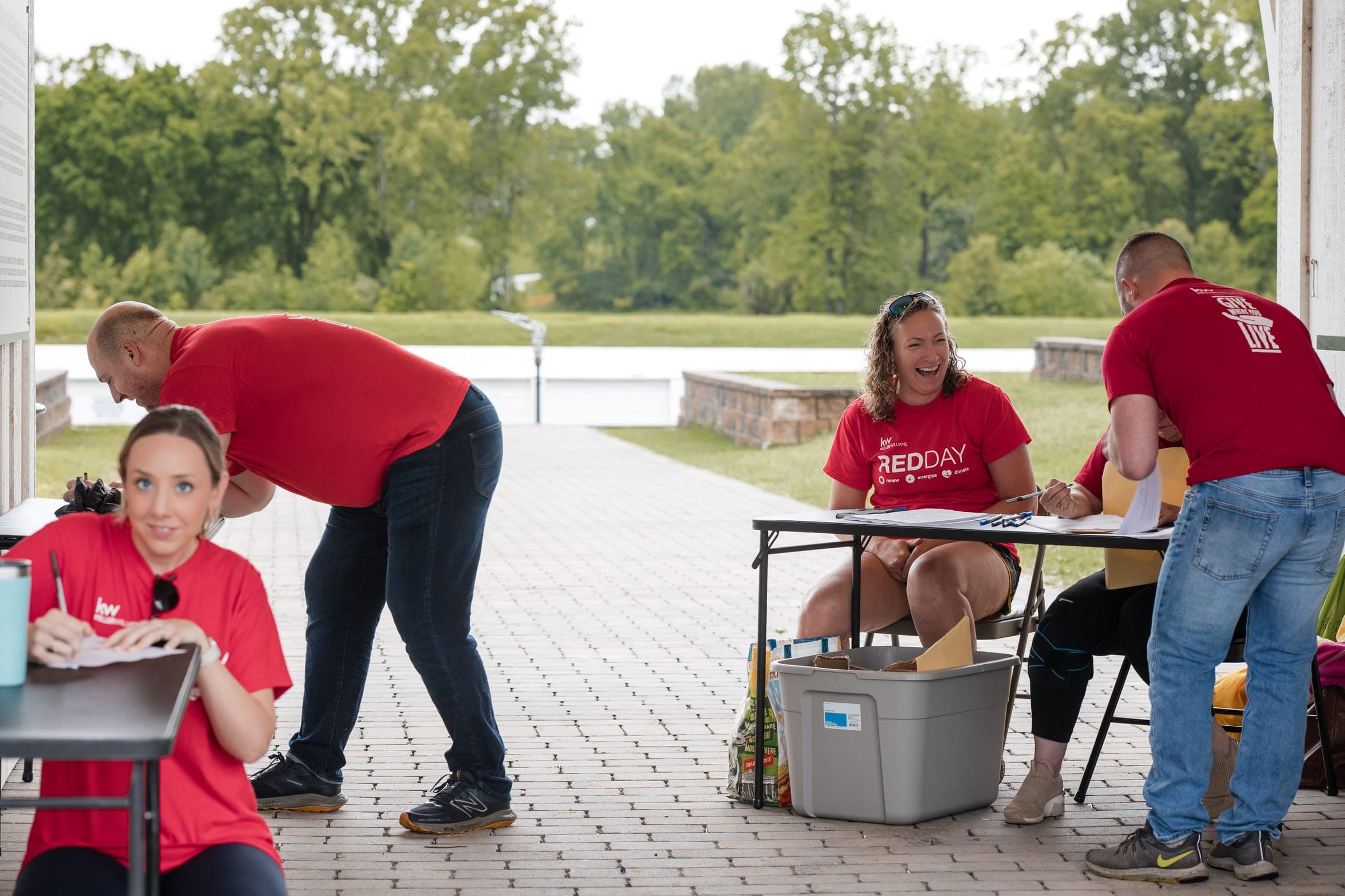 Agents in red shirts laughing at RED Day volunteer sign-up tables in a Franklin park pavilion