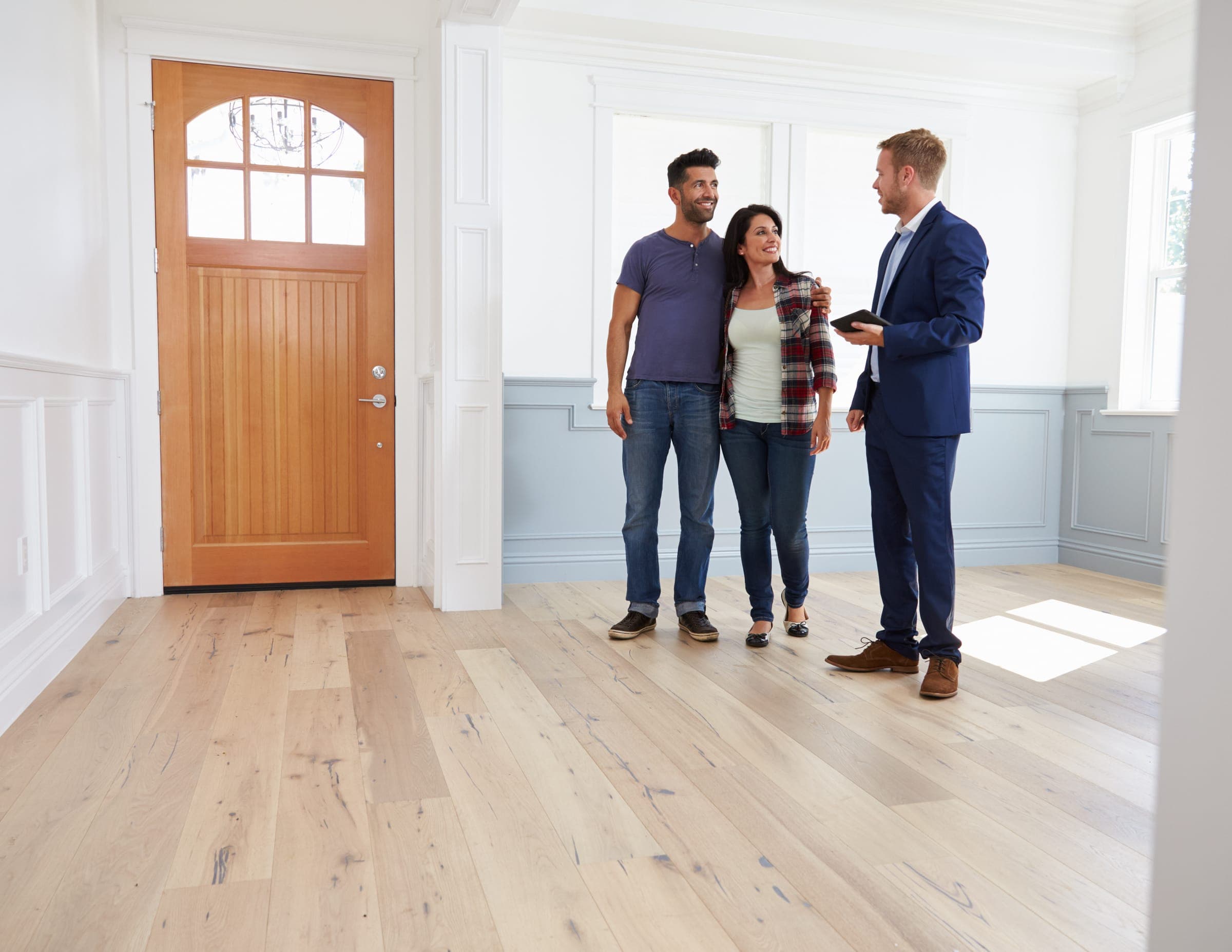 Agent with a tablet walking a smiling couple through a bright, empty home with wide oak floors in Middle Tennessee