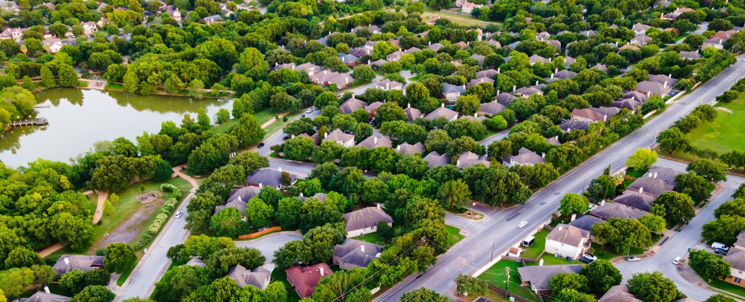 Aerial view of a tree-lined suburban neighborhood curving around a lake at golden hour